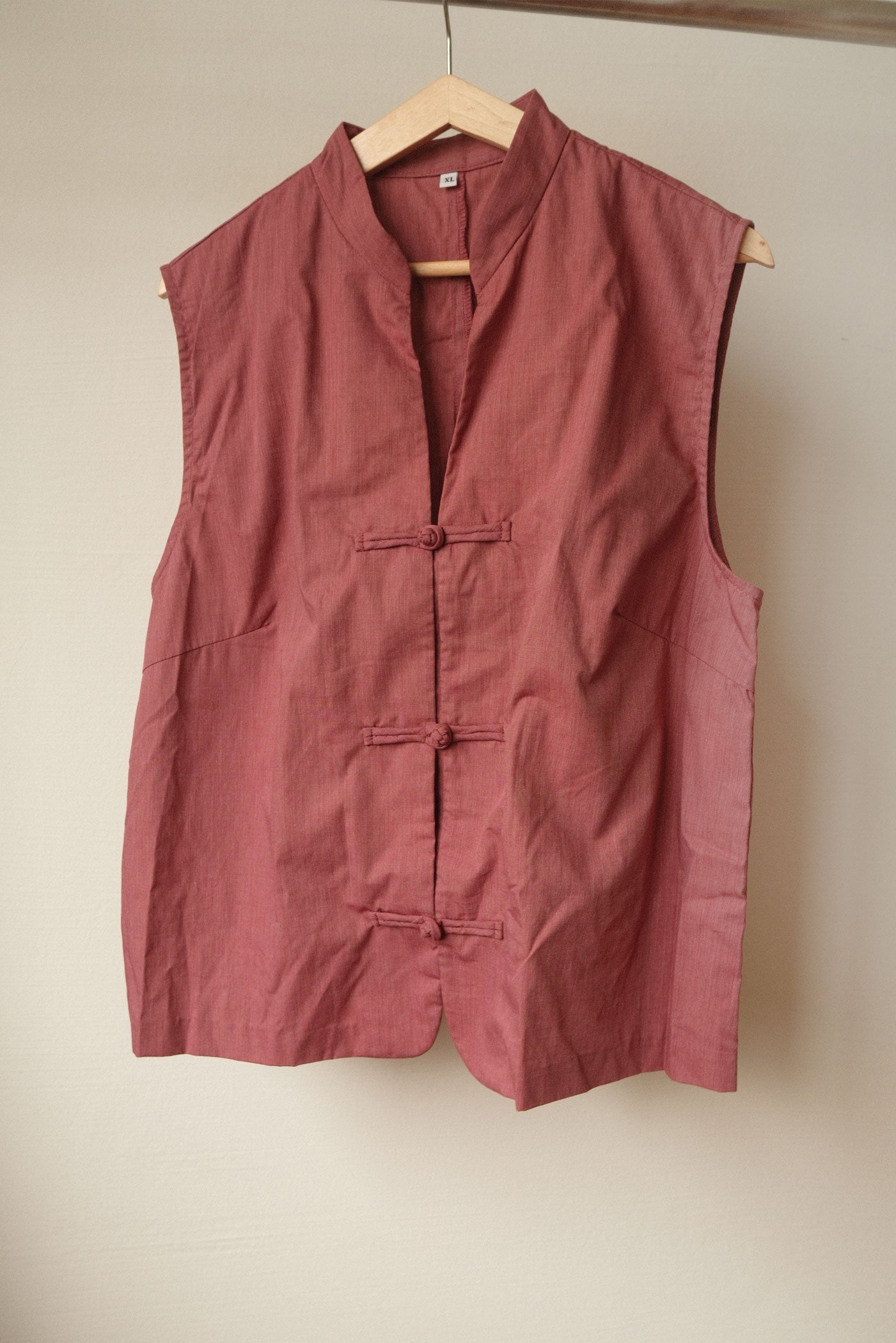 Red sleeveless shirt on a hanger against a beige wall